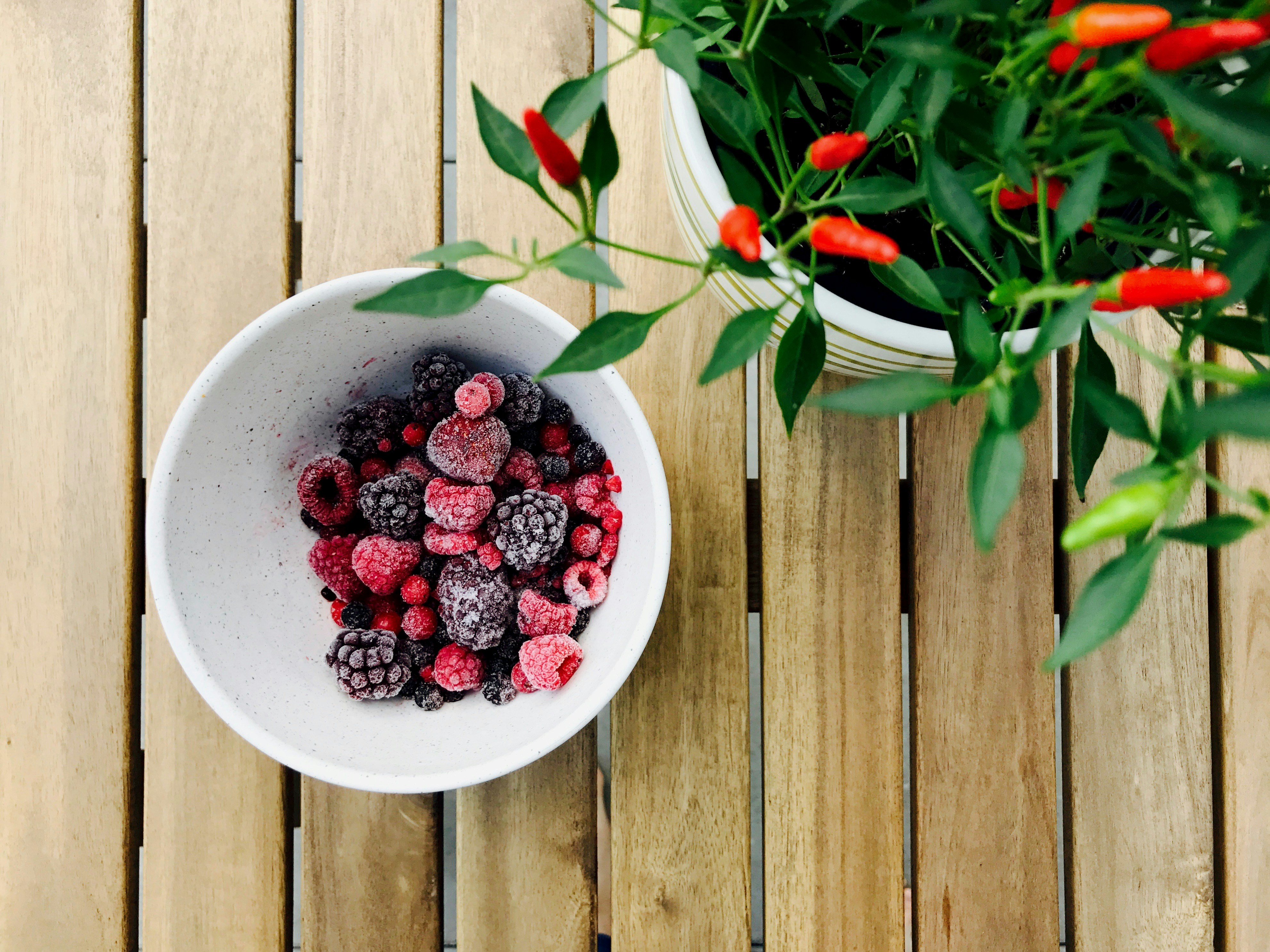 A bowl of frozen mixed berries — raspberries and blackberries dusted with frost — on a wooden table